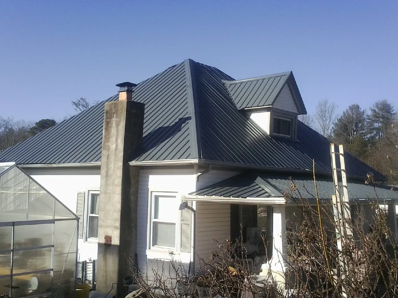 Dark blue standing seam metal roof on a white farmhouse with dormer — Slate & Tile Roof Repair by Roofing Brothers in Sellers