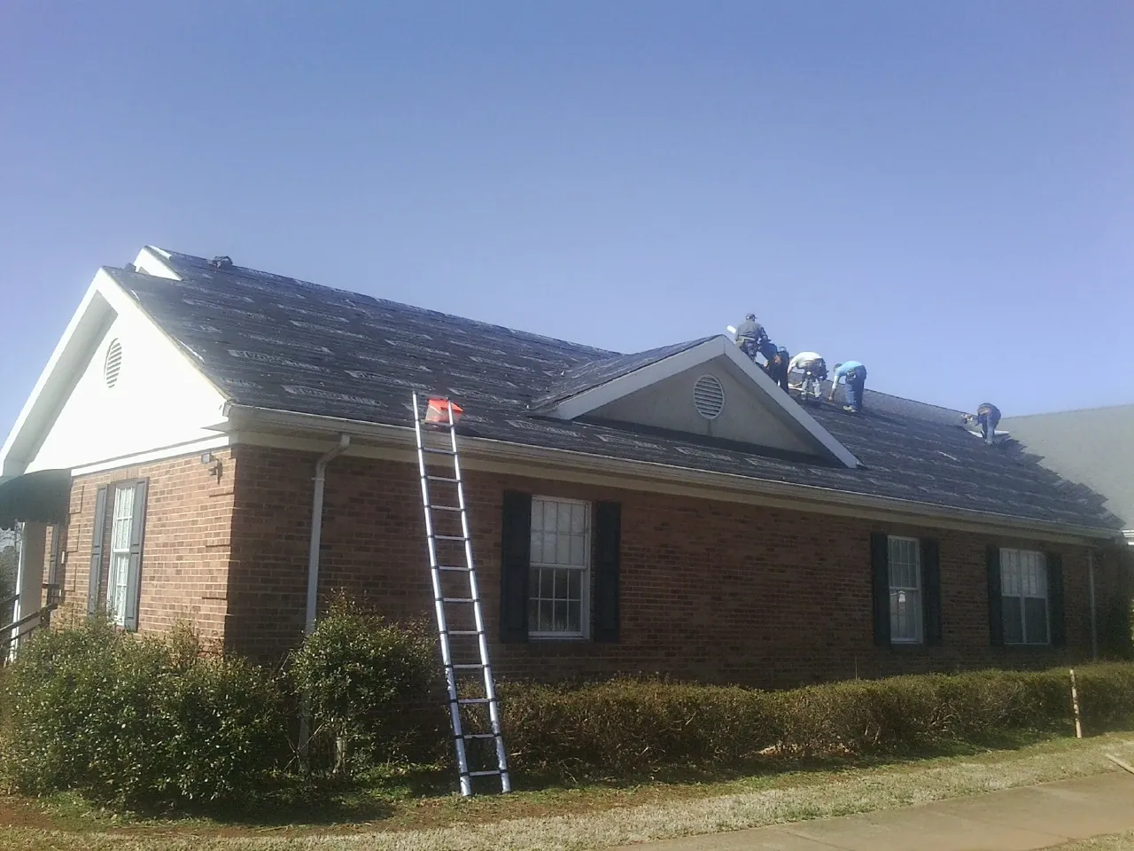 Crew tearing shingles off a brick ranch roof with a ladder set — Metal Roof Repair work by our crew in Sellers
