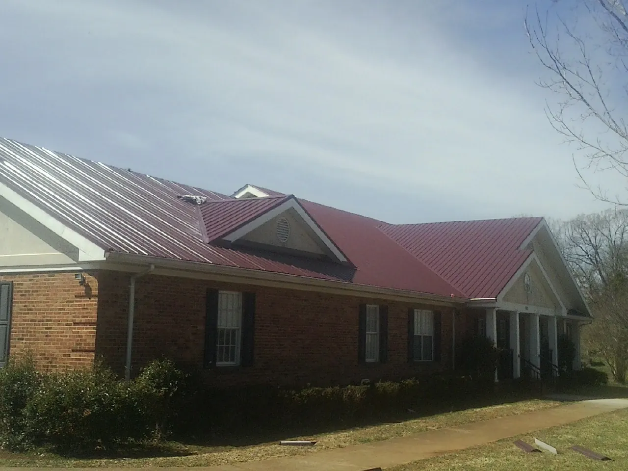 Red metal roof with gabled entries on a long brick building, from a Hail Damage Roof Repair job in Sellers