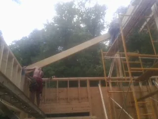 Carpenter raising a rafter beam on a new second story frame in Sellers