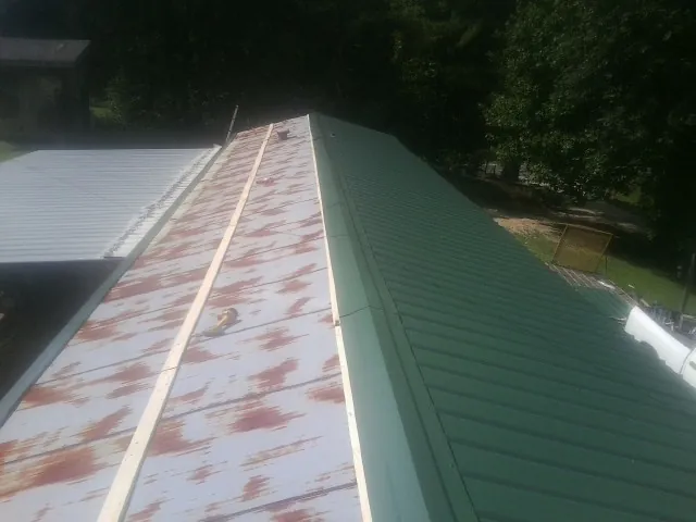 Old rusted panels beside newly installed green metal roofing — Wind Damage Roof Repair by Roofing Brothers in Sellers