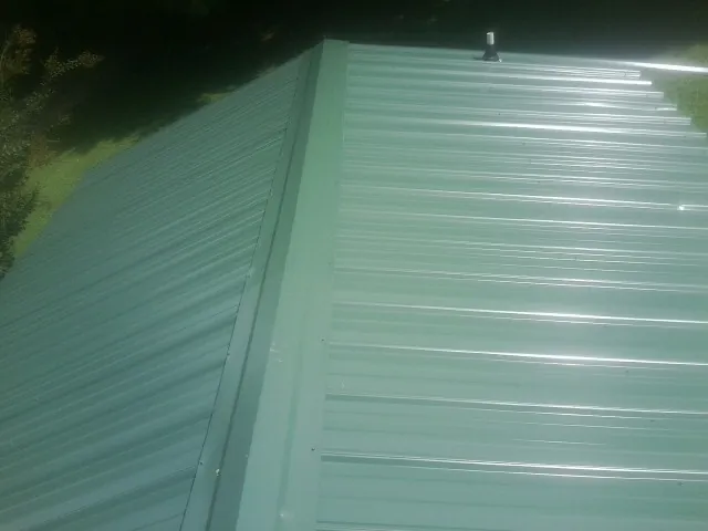 New green metal panels meeting at the ridge of a roof — Flat Roof Repair work by our crew in Sellers