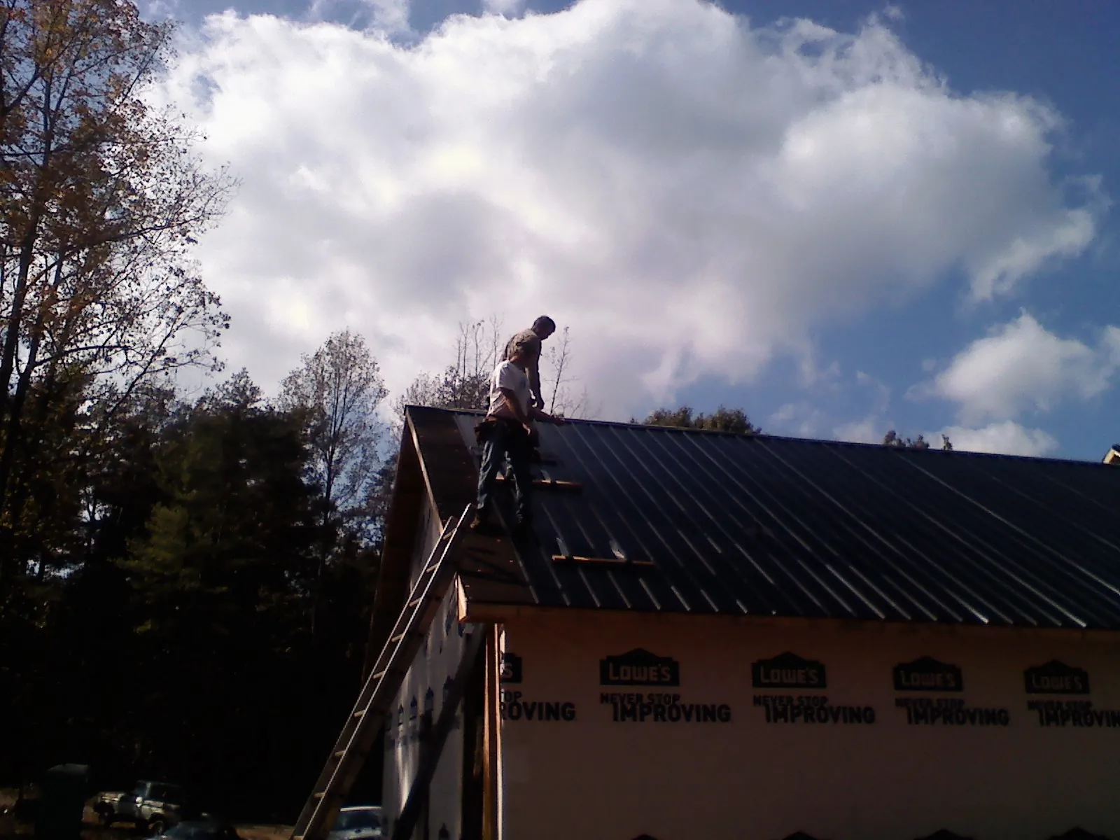 Roofer fastening dark metal panels high against a cloudy sky, from a Roof Inspection job in Sellers