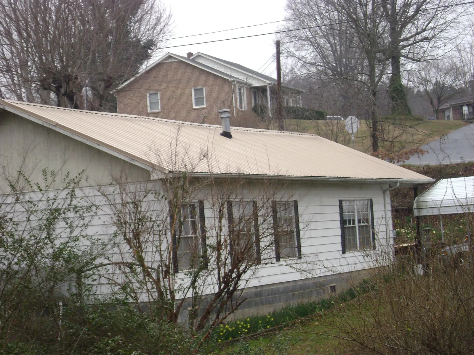 Tan metal roof on a white sided house set into a hillside — Commercial Roofing by Roofing Brothers in Sellers